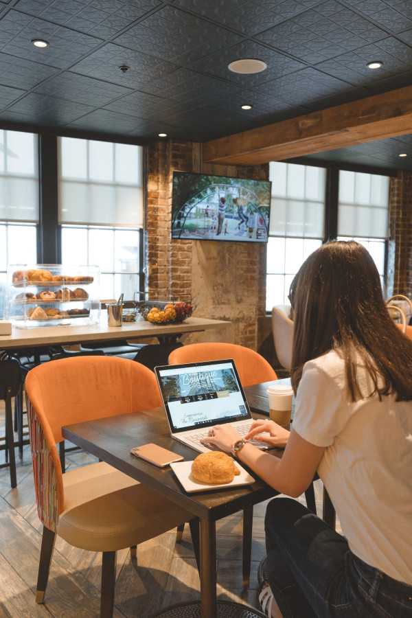 A woman sits at a table in a lobby with a laptop and pastries.