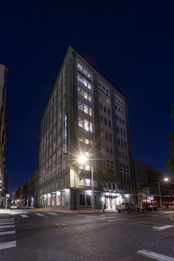A tall building with many windows is seen at night on a city street corner.